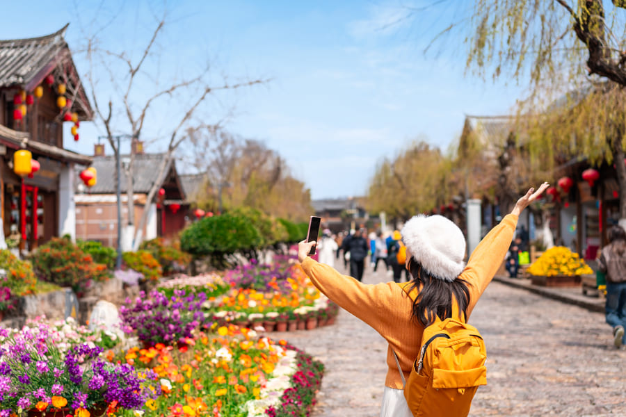 mujer extendiendo los brazon vestida con chamarra amarilla y mochila amarilla viendo un paisaje de flores